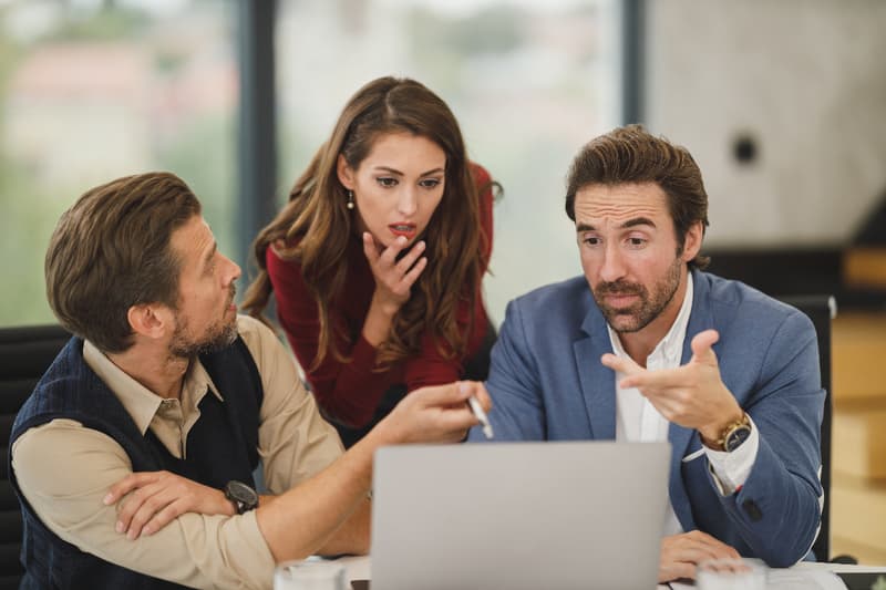 Three colleagues reviewing information together on a laptop in an office.