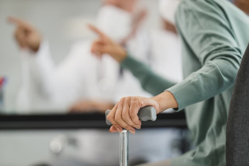 A care worker supporting an older person who is using a walking stick.
