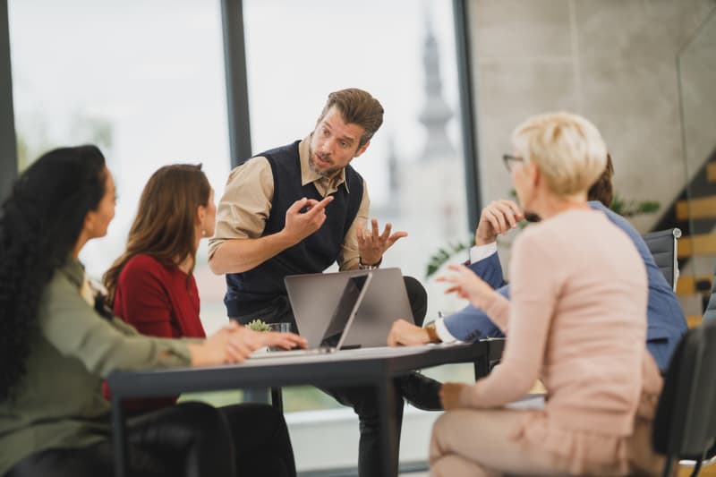 A manager briefing a small team around a meeting table in a bright workplace.