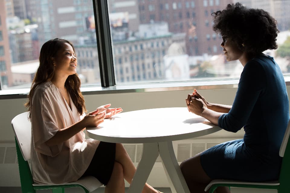 Two people talking across a table in a bright office during a recruitment conversation.
